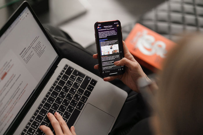 Person scrolling phone while working on laptop